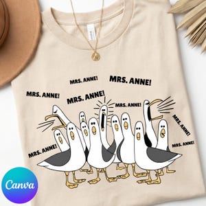 May include: Beige t-shirt featuring a cartoon illustration of seagulls with the text "MRS. ANNE!". The seagulls are white with gray wings and yellow feet. The shirt has a round neckline and short sleeves.