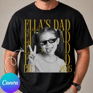 May include: A black t-shirt featuring a large graphic print of a child wearing pixelated sunglasses, sticking out their tongue, and making a peace sign. The background text in gold reads ELLA'S DAD repeated vertically with EST. 2015 at the bottom.
