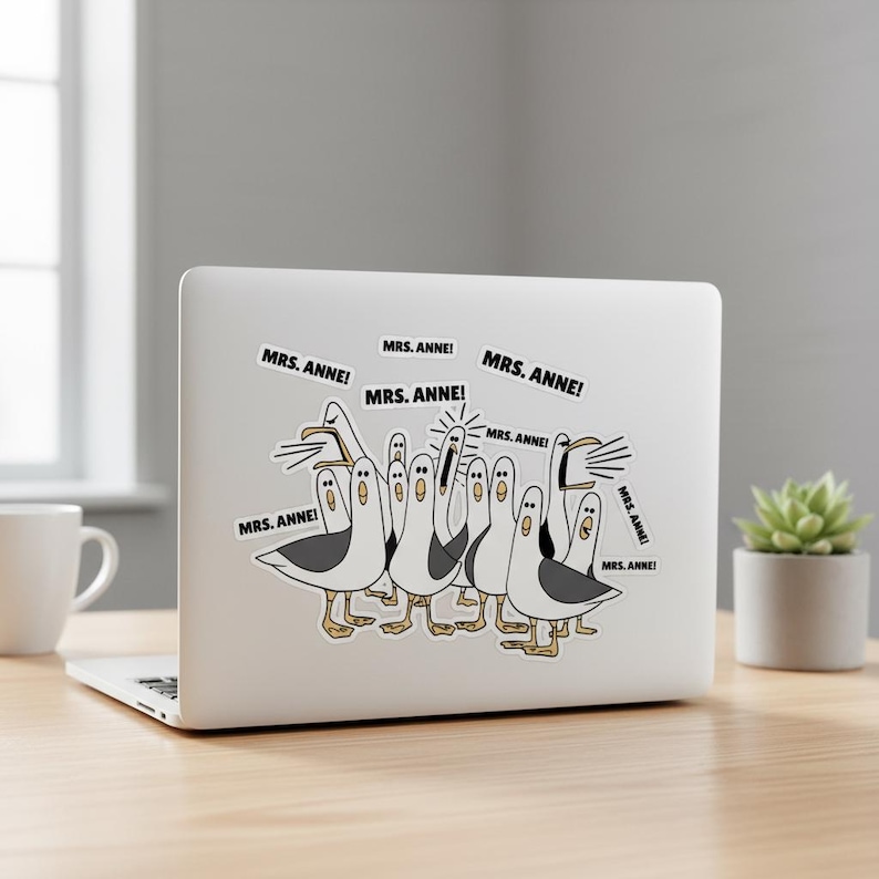 May include: A sticker on a laptop featuring a cartoon illustration of seagulls. The seagulls are white with gray wings and yellow feet. Speech bubbles say "MRS. ANNE!"