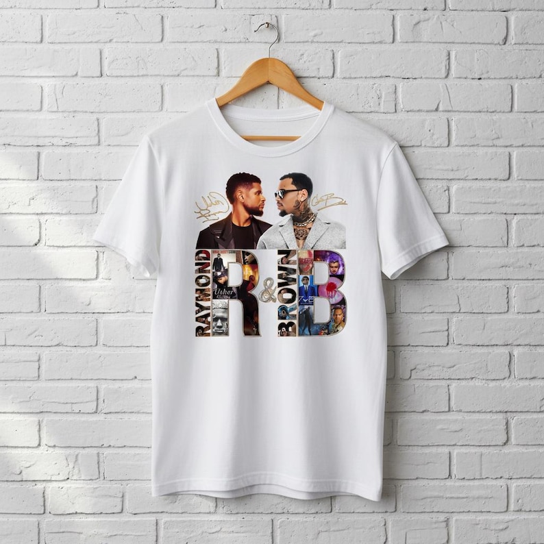 May include: White t-shirt featuring a graphic design with two men facing each other, the text "Raymond & Brown" and images of album covers. The shirt is hanging on a wooden hanger against a white brick wall.