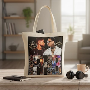 May include: Cream-colored tote bag featuring a graphic of two men with signatures, the words "Raymond" and "Brown", and the letters "R&B". The bag has a rectangular design and a handle.