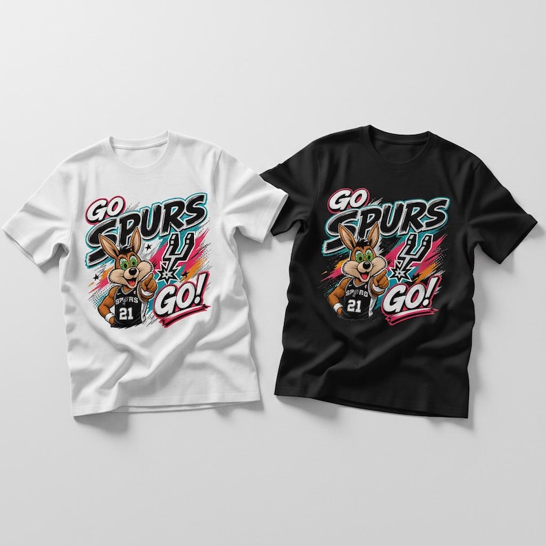 Op de afbeelding: Twee T-shirts met korte mouwen, &eacute;&eacute;n witte en &eacute;&eacute;n zwarte, met een cartoon coyote die een basketbalshirt draagt. De shirts tonen de tekst "GO SPURS GO!" in een kleurrijk ontwerp. De coyote draagt nummer 21.