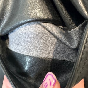May include: Close-up of the inside of a black leather jacket, showing the gray lining. The lining is a soft, smooth fabric.