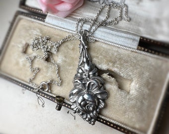 Può includere: Una collana d'argento con un ciondolo a forma di rosa dettagliata. La collana è in una scatola per gioielli foderata in velluto con una rosa rosa in cima.