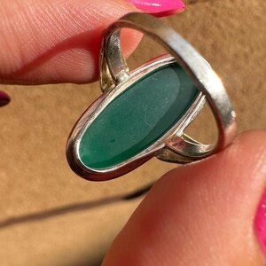 May include: Silver ring featuring an oval, emerald-green gemstone. The ring has a simple, elegant design with a polished finish. The gemstone is set in a bezel setting, and the band is smooth and rounded.
