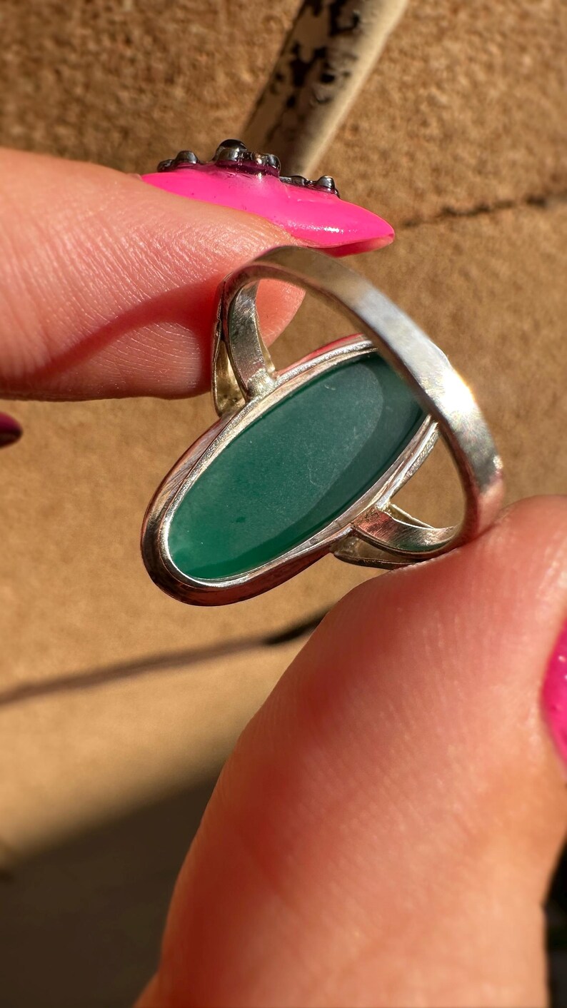 May include: Silver ring featuring an oval, emerald-green gemstone. The ring has a simple, elegant design with a polished finish. The gemstone is set in a bezel setting, and the band is smooth and rounded.