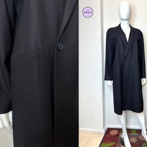 May include: A long black double-breasted coat with a single button closure and a pocket on the left side.
