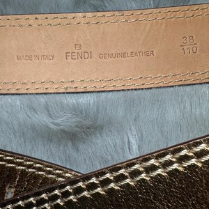 May include: Close-up of a Fendi genuine leather belt. The belt is brown with gold stitching and a gold metallic finish. The belt is marked "Made in Italy" and has the size 38/110.
