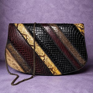 May include: A vintage clutch with a patchwork design. The bag features diagonal stripes in various colors, including black, brown, tan, and yellow. It has a chain strap and a curved bottom edge. The background is a solid purple.