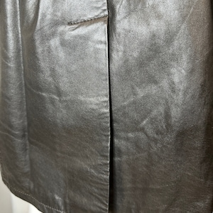 May include: A close-up of a silver leather skirt with a seam down the center back. The skirt has a simple design and a smooth, shiny finish.
