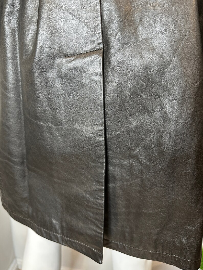 May include: A close-up of a silver leather skirt with a seam down the center back. The skirt has a simple design and a smooth, shiny finish.