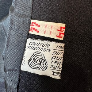 May include: A white label with black text and a black and white logo. The text reads "Compagnie Woolmark" and "Pure New Wool."