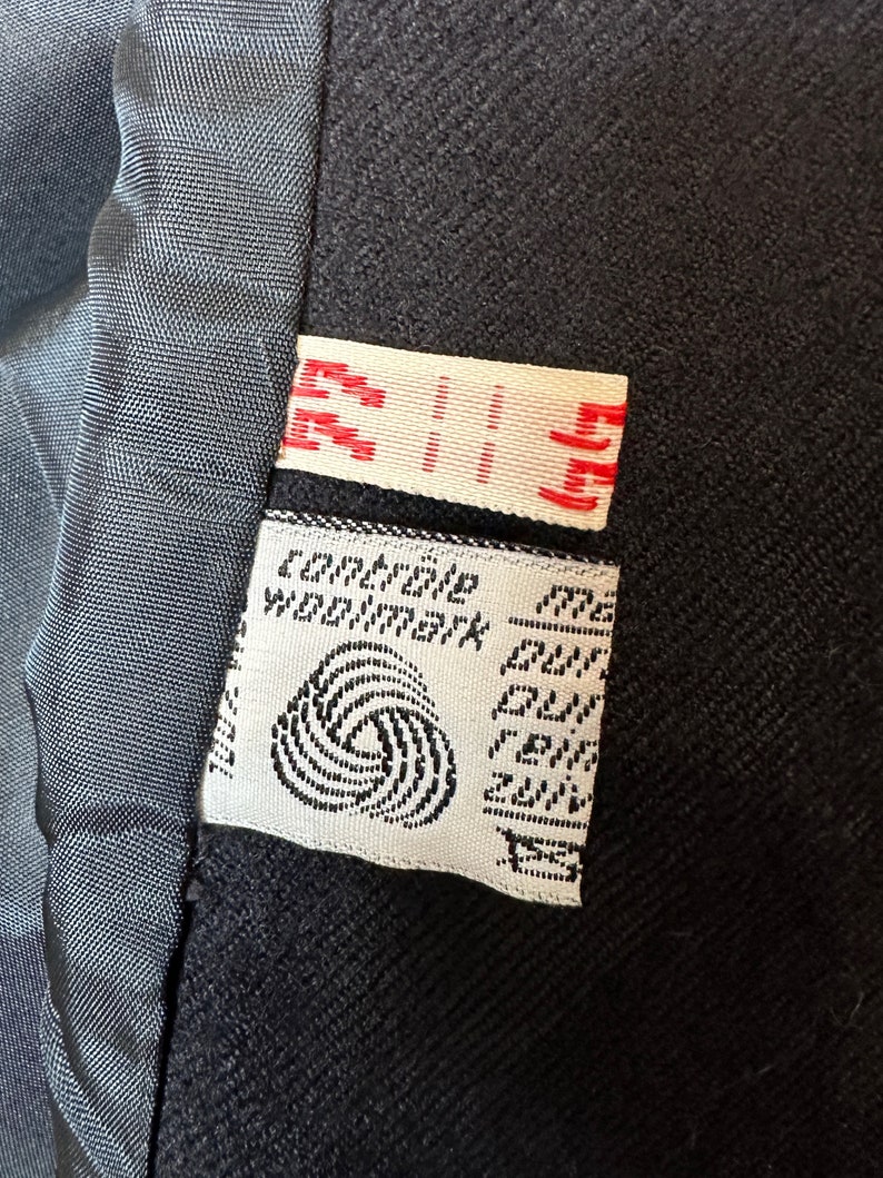 May include: A white label with black text and a black and white logo. The text reads "Compagnie Woolmark" and "Pure New Wool."
