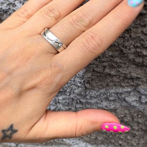 May include: A silver ring with three small clear stones is worn on a finger with colorful, patterned nail polish. The ring has a simple, elegant design. The nails are painted with various colors and polka dots.