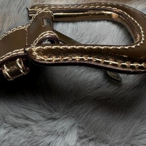 May include: Close-up of a brown leather handle with gold accents and white stitching. The handle is set against a backdrop of gray faux fur, creating a textural contrast. The handle appears to be part of a bag or purse.