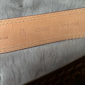 May include: Close-up of a brown leather belt's interior. The belt is stitched with a light-colored thread. The size is indicated as 38 inches and 110 cm. The belt also has the numbers 8C0303 and UP8-068 printed on it.