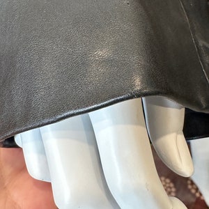May include: Close-up of a black leather jacket sleeve with a textured surface. The sleeve is folded over a white mannequin hand.