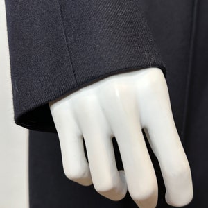 May include: Close-up of a dark blue blazer sleeve with a textured fabric. The sleeve is folded back on itself, revealing the inside of the fabric.