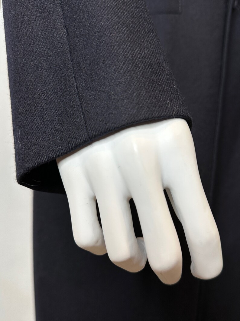 May include: Close-up of a dark blue blazer sleeve with a textured fabric. The sleeve is folded back on itself, revealing the inside of the fabric.