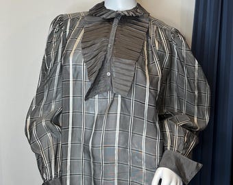 Op de afbeelding: Een grijs en wit geruit blouse met een grote, geplooide ruchekraag. De blouse heeft lange mouwen en een knoopsluiting aan de voorkant.