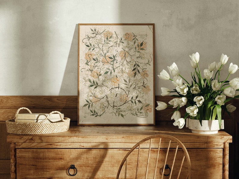 May include: A framed botanical print with a floral design in shades of green, white, and orange. The print is displayed on a wooden dresser with a wicker basket and a vase of white tulips.