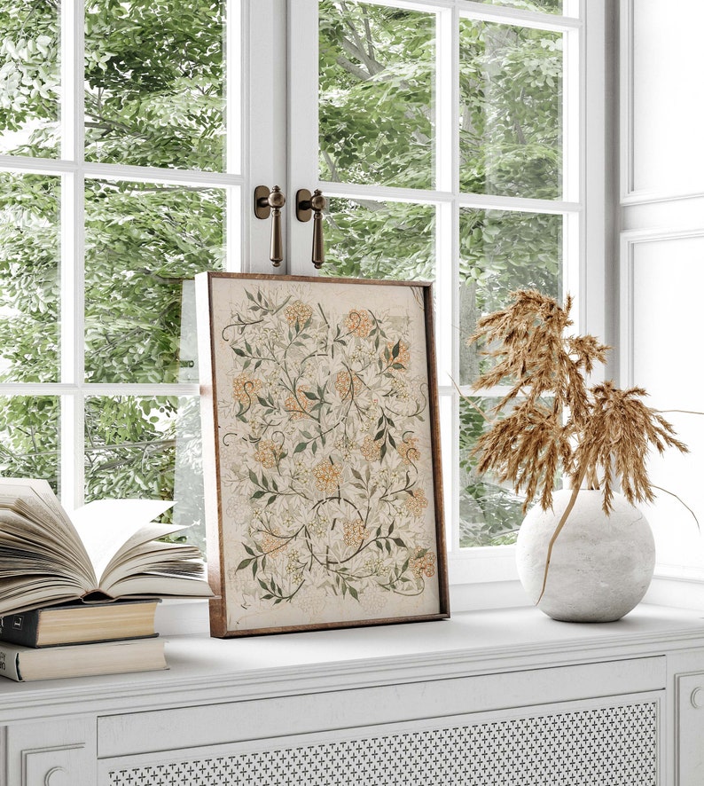 May include: A framed botanical print with a floral design in shades of green, white, and yellow. The print is displayed on a white shelf with a vase of dried grasses and a stack of books.