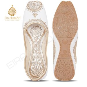 May include: A pair of white slip-on shoes featuring intricate gold embroidery on the upper surface and a tan rubber sole with a floral tread pattern. The interior insole is also decorated with matching gold embroidery. The size 10 is visible.