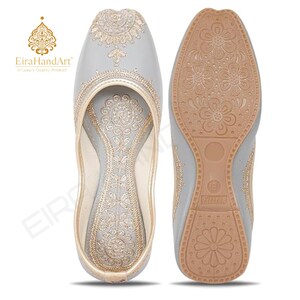 May include: A pair of light grey slip-on shoes featuring intricate gold embroidery on the upper and inner sole. The outer sole is tan with a floral pattern and the number 8 embossed on the heel. The EiraHandArt logo is visible in the corner.