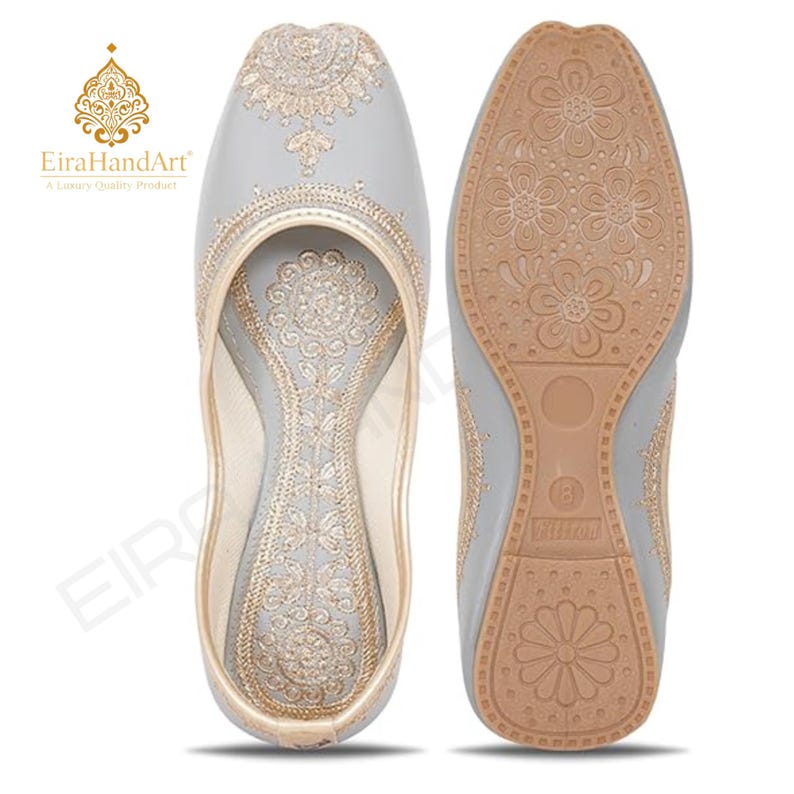 May include: A pair of light grey slip-on shoes featuring intricate gold embroidery on the upper and inner sole. The outer sole is tan with a floral pattern and the number 8 embossed on the heel. The EiraHandArt logo is visible in the corner.
