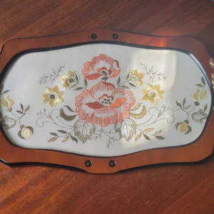 Vintage tray with hand stitched flowers under glass. Encased in wood. Ornate metal handles.