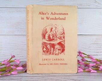 Puede incluir: Una copia vintage de "Alice's Adventures in Wonderland" de Lewis Carroll. El libro tiene una portada color crema con texto e ilustraciones en rojo. El título se muestra de forma destacada, con los nombres del autor e ilustrador debajo.