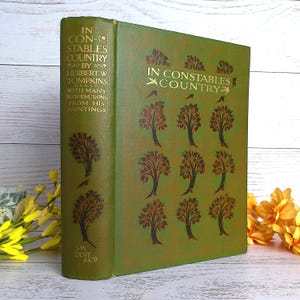 May include: A hardcover book titled "IN CONSTABLES COUNTRY" by Herbert W. Tompkins. The book has a green cover with gold lettering and tree illustrations. The spine also features text and tree designs. The book is a vintage item.