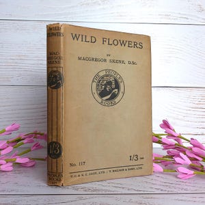 Könnte beinhalten: Ein Vintage-Buch mit dem Titel "Wild Flowers" von Macgregor Skene, D.Sc. Das Cover ist beige mit schwarzem Text und einem kreisförmigen Emblem. Der Buchrücken zeigt den Titel und den Namen des Autors. Das Buch gehört zur Reihe "The People's Books".