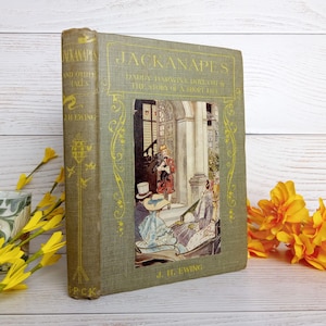 Op de afbeelding: Antiek hardcover boek getiteld "Jackanapes and Other Tales" van J.H. Ewing. Het boek heeft een groene kaft met gouden letters en illustraties. De omslagillustratie toont een scène met figuren en een hond. De rug van het boek is ook groen met gouden accenten.