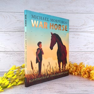 May include: A hardcover book titled "War Horse" by Michael Morpurgo, illustrated by Tom Clohosy Cole. The cover features a boy and a horse in a field at sunset. The title is in large, copper-colored letters.