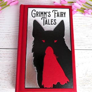 May include: A red hardback book titled "Grimm's Fairy Tales." The cover shows a black wolf silhouette with red eyes and a red-caped figure. The book has a silver background and a red border.
