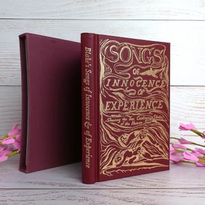 May include: A maroon book titled "Songs of Innocence and of Experience" with gold lettering and illustrations. The book is in a maroon slipcase. The spine reads "Blake's Songs of Innocence & of Experience".