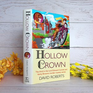 Può includere: Un libro con copertina rigida intitolato "Hollow Crown" di David Roberts. La copertina presenta un'illustrazione colorata di una persona in moto, una casa signorile e il titolo del libro. Il dorso mostra il titolo e il nome dell'autore.