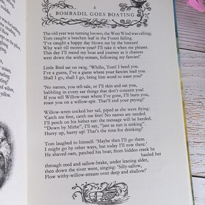 Op de afbeelding: Open boek met tekst en illustraties. De pagina toont de titel "Bombadil Goes Boating" en een decoratieve illustratie. De tekst beschrijft een verhaal over Tom en zijn reis. Roze bloemen zijn zichtbaar op de achtergrond.