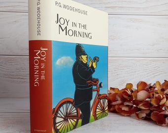 May include: A book titled "Joy in the Morning" by P.G. Wodehouse. The cover features a cartoon illustration of a police officer on a bicycle.