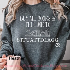 May include: Dark heather grey sweatshirt with the text "Buy me books & tell me to STFUATTDLAGG" in white. The sweatshirt features a graphic of a bookshelf with books and a plant.