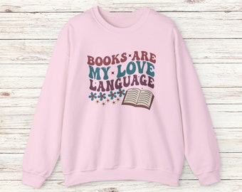 May include: Pink sweatshirt with the text "BOOKS ARE MY LOVE LANGUAGE" in a retro font with a book and flowers.