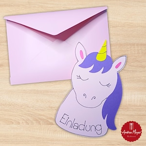 Könnte beinhalten: Eine hellviolette Einladungskarte in Form eines Einhornkopfes mit dem Wort "Einladung" und einem passenden Umschlag. Das Einhorn hat ein gelbes Horn, eine lila Mähne und geschlossene Augen. Der Hintergrund ist eine helle Holzoberfläche.
