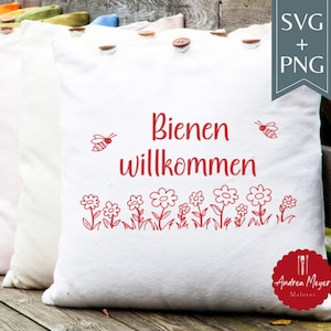 May include: White pillow with red text that reads "Bienen willkommen" and a floral design. The pillow has a bee graphic and is decorated with wooden buttons. The pillow is part of a set.