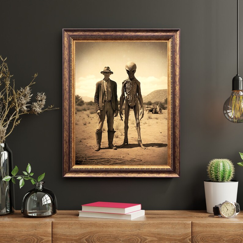 May include: A black and white photograph of a man in a cowboy hat standing next to a tall, thin alien with a large head. The man is wearing a long-sleeved shirt and pants. The alien has a skeletal appearance and is wearing a long, flowing robe. The photo is framed in a brown wooden frame.