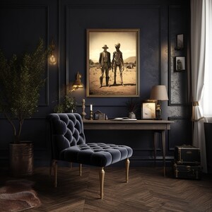 May include: A dark blue velvet armchair with tufted upholstery sits in a dark room with a wooden desk and a framed print of two figures in a desert landscape. The print features a man in a hat and a tall, slender figure with a large head.