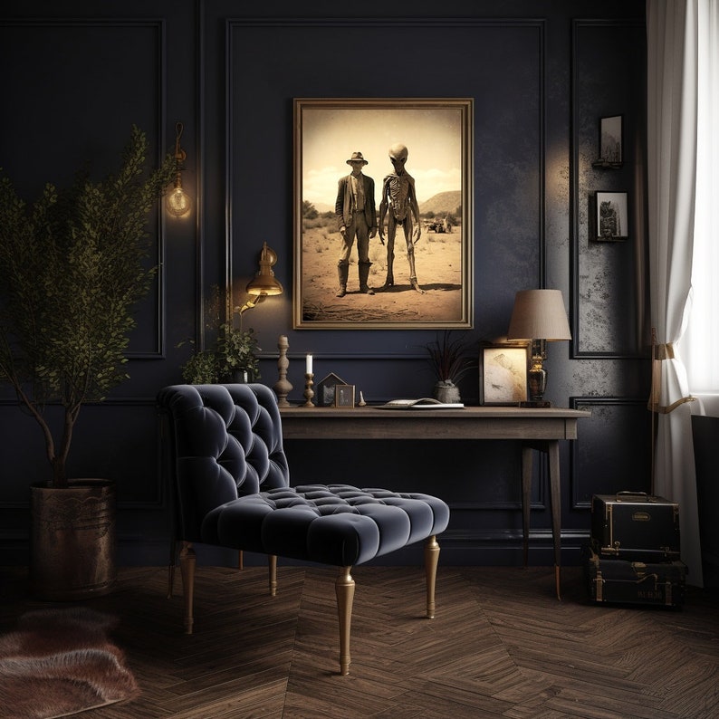 May include: A dark blue velvet armchair with tufted upholstery sits in a dark room with a wooden desk and a framed print of two figures in a desert landscape. The print features a man in a hat and a tall, slender figure with a large head.