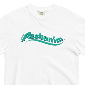 Könnte beinhalten: Weißes T-Shirt mit einem grün-blauen Logo, auf dem in einer wellenförmigen Schrift "Pashanim" steht.