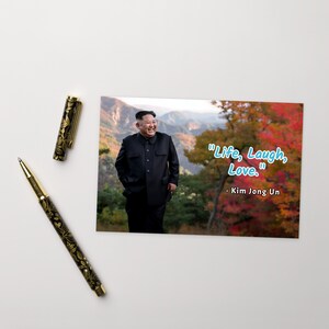 Könnte beinhalten: Ein Schwarzweißfoto eines Mannes im schwarzen Anzug, der vor einer Bergkette mit Herbstlaub steht. Das Zitat "Life, Laugh, Love." ist in blauer Schrift unter dem Mann geschrieben. Das Zitat wird Kim Jong Un zugeschrieben.