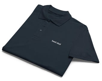 Op de afbeelding: Marineblauwe polo met kraag en drie knopen. De tekst "best dad" is wit op de voorkant geborduurd. De polo is opgevouwen, wat suggereert dat het nieuw is.